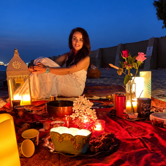 Woman seated by glowing lanterns at a beach gathering